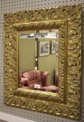 A contemporary wall mirror. The carved wooden frame finished in gold, H65cm x W57cm.