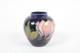 A small Moorcroft tube lined vase. Decorated with flowering magnolia sprigs on a dark blue ground.