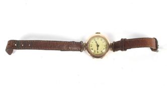 A vintage 9ct gold cased watch on a narrow leather strap. With Arabic numerals on a yellowish face.