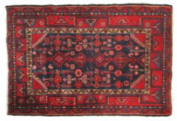 A Persian Hamadan floor rug with red ground and central blue field within geometric borders.