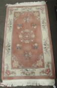 A Chinese style rug. Decorated with floral details on a pink and cream ground.