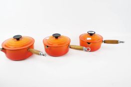A set of three orange enamel Le Creuset saucepans and lids. Sizes 16, 18 & 20.