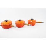 A set of three orange enamel Le Creuset saucepans and lids. Sizes 16, 18 & 20.