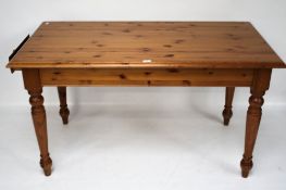 A pine kitchen table. With a drawer at one end, on turned supports.