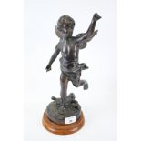 A cast figure of a standing cherub on a circular wood base.