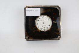 A travelling clock in a silver and tortoise shell case.