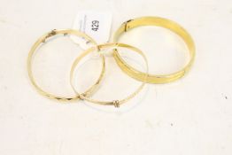 Three gold-plated bangles. Comprising; a facetted hinged bangle marked '1/5th 9ct R.G.