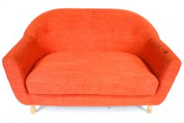 A contemporary orange two seater sofa. Raised on turned supports.