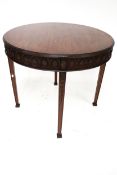 A circular dining table. With a carved frieze on tapering square supports and square feet.