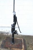 A very large cast iron well water pump. Painted black, mounted on board.