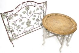 A brass tray top folding table and a metalwork screen with candles.