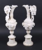 A large pair of cream alabaster ewers with fruiting vine decoration and raised on round socles.