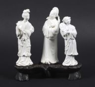 Three Chinese blanc de chine figures mounted on a carved wood base.