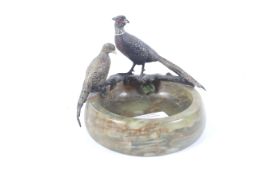 A circular onyx ashtray decorated with painted lead figures of a cock and hen pheasant.