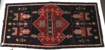 An Iranian hand made wool rug. With traditional Persian decoration, red on a dark blue ground.