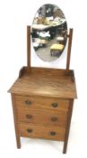 A vintage oak chest of three drawers with an oval mirror.
