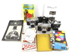 An assortment of cameras, lenses, photography books and camera manuals.