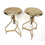 A pair of brass finish adjustable stools. On tripod supports.