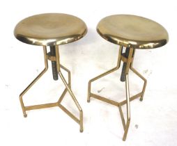 A pair of brass finish adjustable stools. On tripod supports.