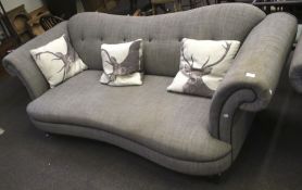 A contemporary grey upholstered three seater sofa with scroll arms. On turned tapering supports.