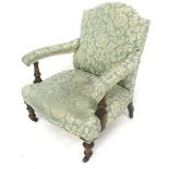 A low open upholstered armchair. Hump back, on turned tapering supports with casters.