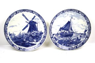 A pair of Delft blue and white chargers. One depicting a windmill, the other a boat.