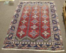 A Persian style wool rug with red and blue ground. Geometric border and central decoration.