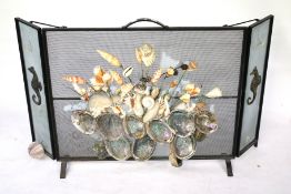 A mid-century wrought iron folding fire screen. Guard later decorated with mixed seashells.