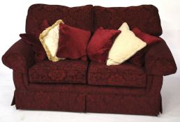 A two-seater maroon sofa with extra cushions.