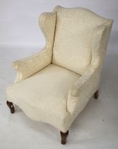 A wingback armchair upholstered in cream fabric, on shaped supports.
