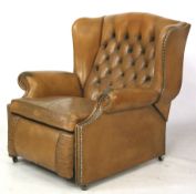 A vintage tan leather reclining button back armchair. With brass studded scroll arms on casters.