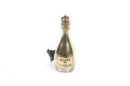 An early 20th century novelty brass cased tape measure in the form of a bottle of Veuve Cliquot