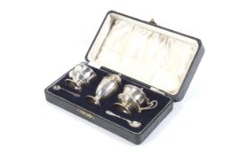 A silver three piece round pedestal cruet set and two spoons.