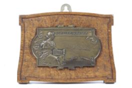 A cast metal plaque of a lady holding a camera. With text reading 'Photography' and 'W.H.