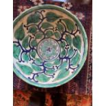 An old Eastern earthenware bowl decorated overall with stylised flowering foliage in green & blue on