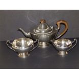 An Arts & Crafts three piece crested silver bachelor's tea service of circular plan, the upturned