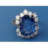 A modern sapphire & diamond set cluster ring, the oval claw set sapphire weighing approximately 4