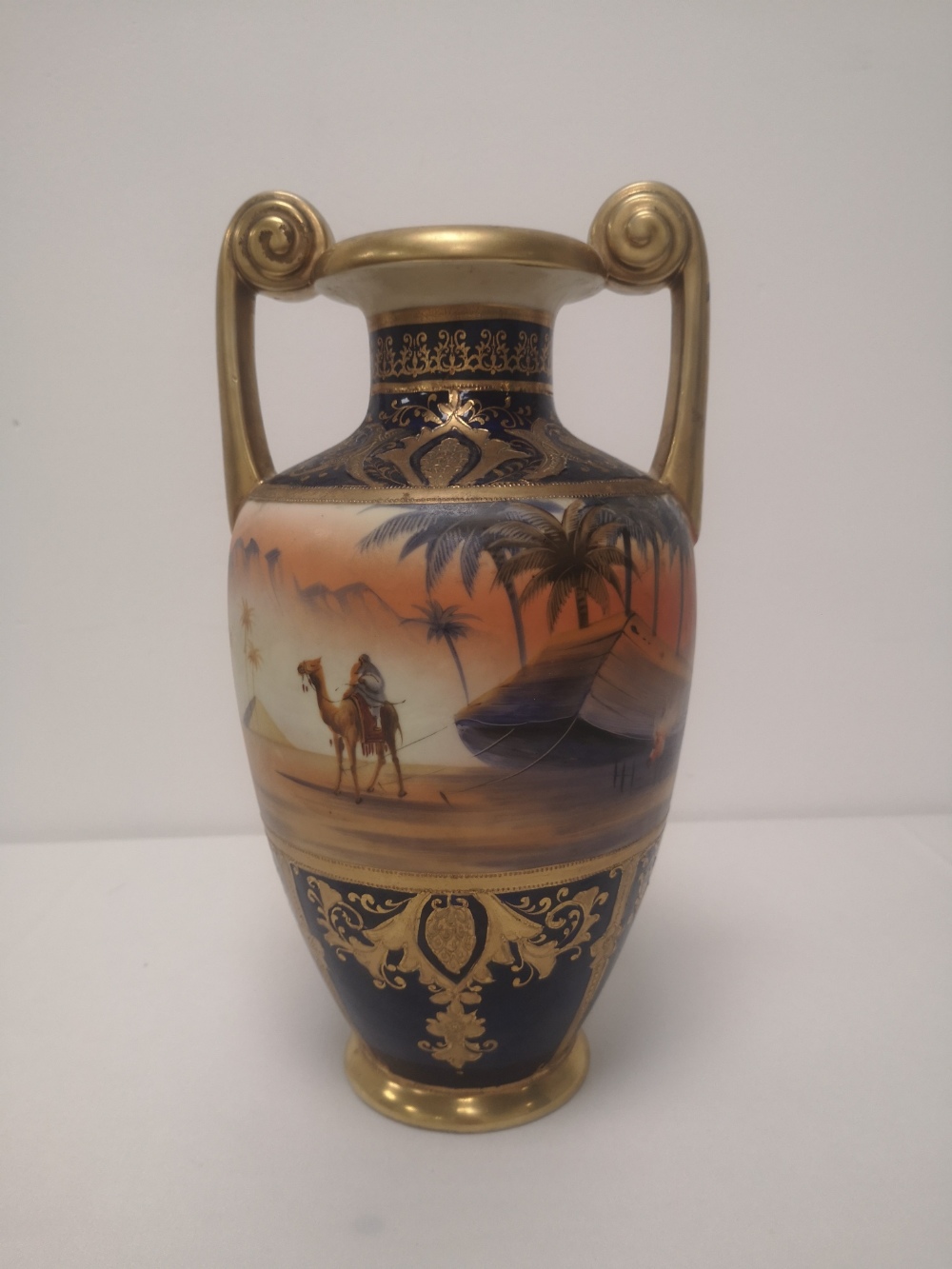 A Noritake vase painted with a camel in desert scene, 11" high.