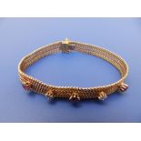A yellow metal bracelet of chainmail design, claw set with two small diamonds and three rubies -