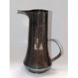 A plain white metal water jug by Christopher Gibson, of spreading cylinder form with low set loop