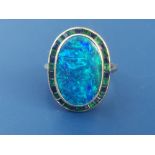 An opal, emerald & sapphire cluster ring, the oval opal within a border of calibre set alternating