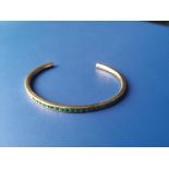 An emerald set 18ct gold bangle, of open-ended hoop form, maximum internal dimension approximately