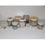Seven jars containing small quantities of very small faceted gemstones including garnets, emeralds &