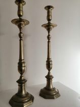 A pair of tall antique brass candlesticks, having drip pans above slender stems to octagonal