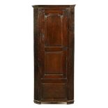 An 18th century oak freestanding corner cupboard, with central fielded cupboard door,