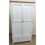 A modern white wood wardrobe with two cupboard doors over a single drawer,