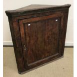 An 18th Century dark stained pine hanging corner cupboard with single door enclosing a painted