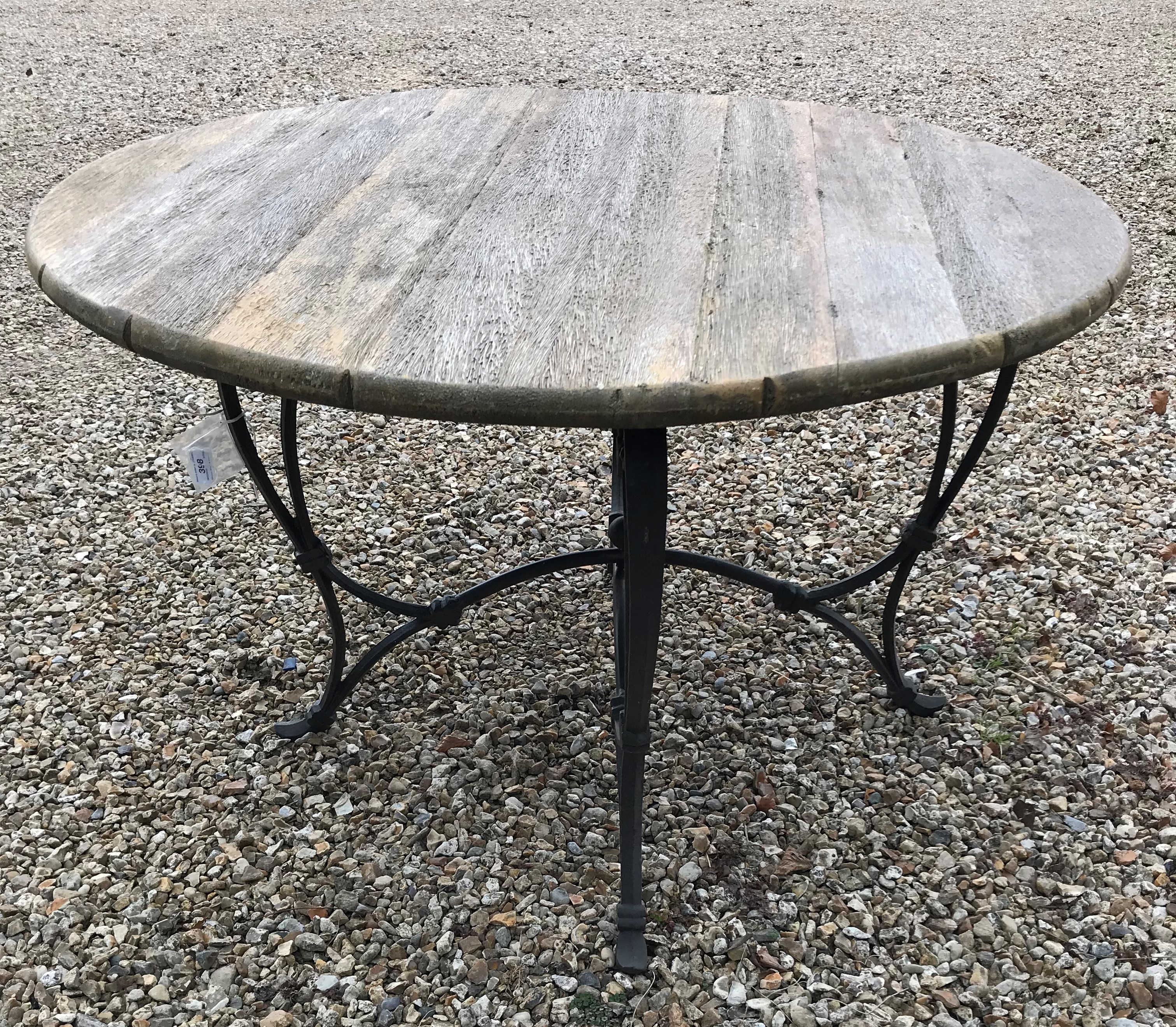 A garden table, the weathered wooden circular top above a painted cast metal base of scrolling form,