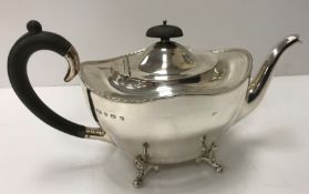 A George V silver teapot on four scroll feet and with ebonised handles (by William Suckling Ltd,