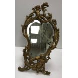 A brass easel mirror of shaped form in the Rococo taste with bevel edge plate,